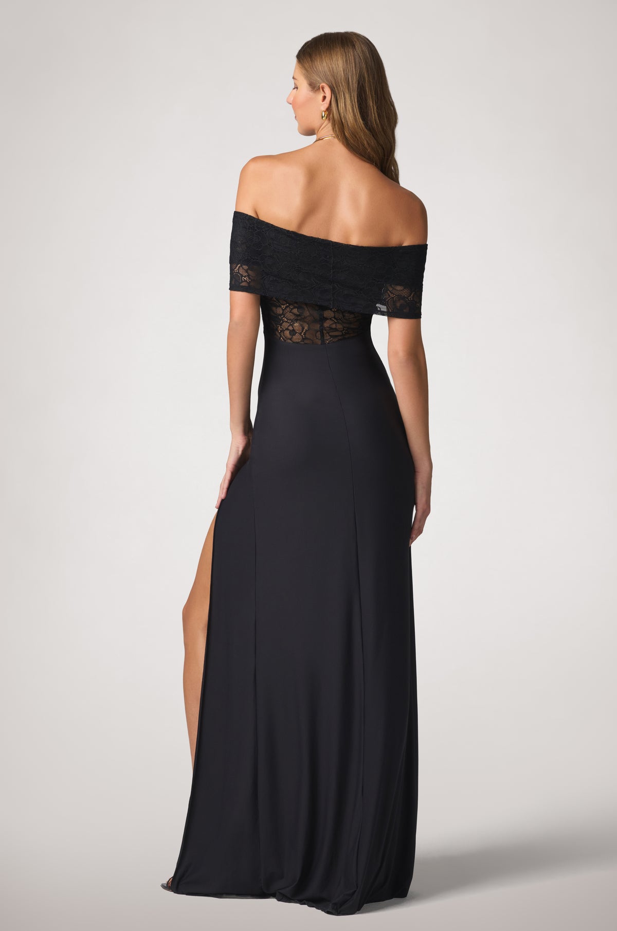 Elegant off-the-shoulder back with floral lace framing the upper body and a sleek, floor-length jersey silhouette flowing toward the hem.